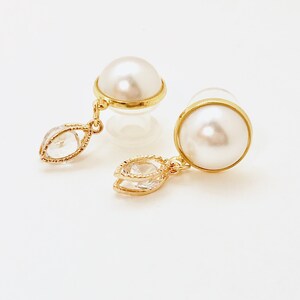 May include: A pair of gold earrings with a pearl and a clear crystal drop. The earrings are on a white background.