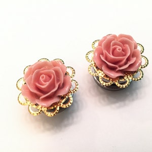 K&ouml;nnte beinhalten: Ein Paar Ohrstecker in Form einer rosa Rose mit goldenen Filigran-Akzenten. Die Ohrstecker sind aus Metall und haben eine glatte Oberfl&auml;che.