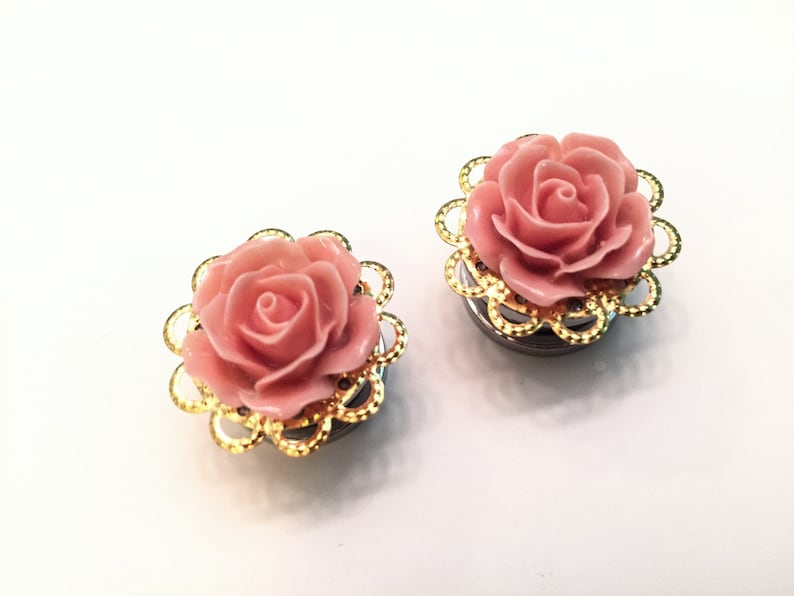 K&ouml;nnte beinhalten: Ein Paar Ohrstecker in Form einer rosa Rose mit goldenen Filigran-Akzenten. Die Ohrstecker sind aus Metall und haben eine glatte Oberfl&auml;che.