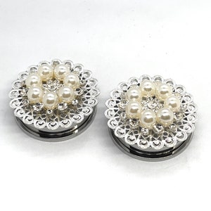 May include: A pair of silver ear gauges with a decorative filigree design and white pearl accents.