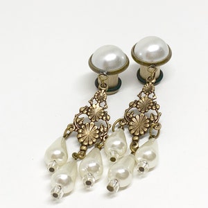 May include: A pair of gold-tone earrings with a pearl design. Each earring features a large faux pearl, a dangling floral design, and several smaller faux pearls.