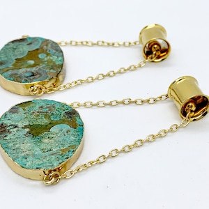 May include: A pair of gold-toned ear gauges with a green and blue agate stone attached to each gauge. The stones are connected to the gauges by a gold chain.