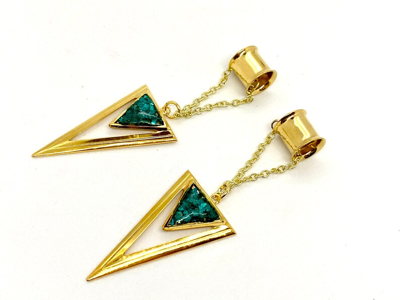 May include: A pair of gold-colored earrings featuring a geometric design. Each earring has a triangular shape with a turquoise-colored stone inlay and a chain connecting to a cylindrical post.