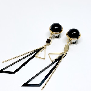 May include: A pair of black and gold geometric dangle earrings. The earrings feature a black sphere with a gold rim and a dangling chain with black and gold triangles.