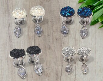 Puede incluir: Un juego de seis expansores de oreja plateados con colgantes de cristal. Los expansores están disponibles en tres colores diferentes: blanco, negro y azul.