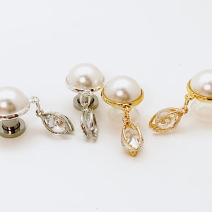 May include: Three pairs of pearl earrings with dangling crystal charms. The earrings are in silver, gold, and gold with a silver charm.
