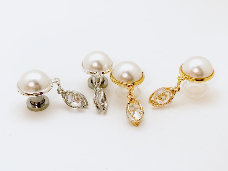 May include: Three pairs of pearl earrings with dangling crystal charms. The earrings are in silver, gold, and gold with a silver charm.