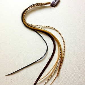 May include: A hair feather extension with a metal clip. The feathers are a mix of black, brown, tan, and yellow. The clip is silver and has a small, decorative design.