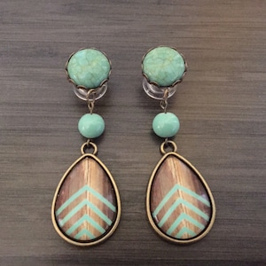May include: A pair of turquoise and brown dangle earrings with a teardrop-shaped wooden charm featuring a green chevron pattern.