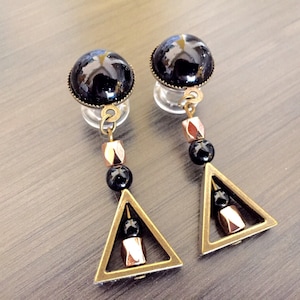 May include: A pair of black and gold dangle earrings with a black glass bead and a triangle pendant. The triangle pendant has a gold frame and a black bead inside.