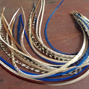 May include: A bundle of long, thin feathers in shades of white, brown, and blue. The feathers are arranged in a loose, flowing pattern.