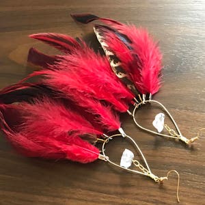 May include: A pair of red feather earrings with gold hoops and clear crystal accents.