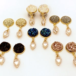 May include: Set of 10 pairs of gold-tone dangle earrings with various colours of glitter-filled round stones. Each earring features a clear crystal teardrop dangle.