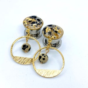 May include: A pair of gold and black patterned ear gauges with dangling gold hoops and black and white stone accents.