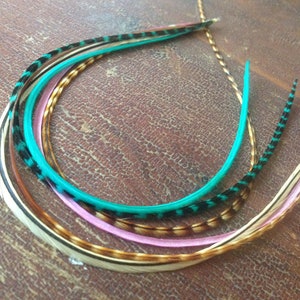 以下が含まれることがあります： ターコイズ、ピンク、ブラウン、ホワイトなど、さまざまな色のフェザーヘアエクステンション4本セット。フェザーは円形に配置され、ターコイズのフェザーが上部に位置しています。