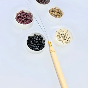 May include: Five containers of micro rings for hair extensions in black, brown, light brown, blonde, and white. A wooden tool with a gold tip is also pictured.