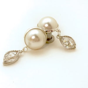 May include: A pair of white pearl earrings with a clear crystal dangle. The earrings are silver-toned and have a simple design.