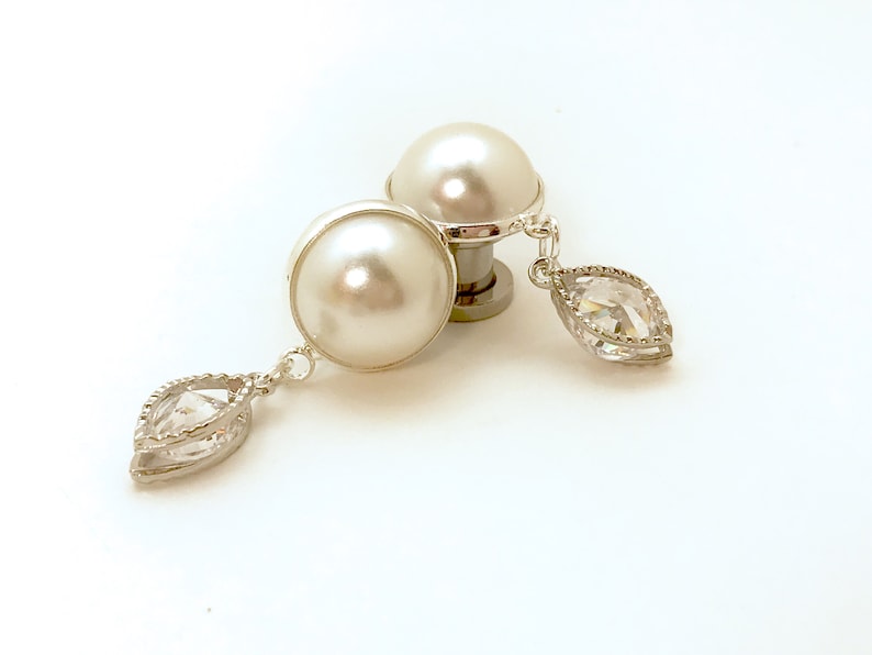 May include: A pair of white pearl earrings with a clear crystal dangle. The earrings are silver-toned and have a simple design.