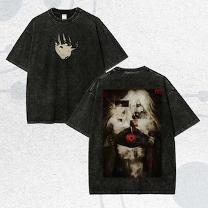Könnte beinhalten: Doppelseitiges schwarzes T-Shirt mit verwaschenem Vintage-Look. Auf der Vorderseite ist ein stilisiertes Gesicht abgebildet, während die Rückseite eine detaillierte, künstlerische Illustration von zwei Figuren mit einem roten Zentralelement zeigt. Das T-Shirt hat kurze Ärmel und einen Rundhalsausschnitt.