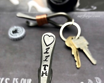 May include: A silver bottle opener with a heart and the name "Lizzy" engraved on it. The opener is wrapped with a copper wire coil.