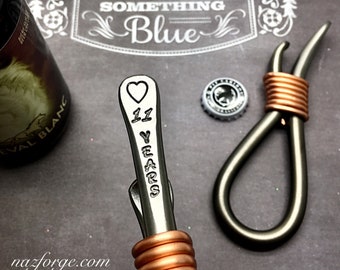 May include: A metal bottle opener with a copper-wrapped handle, stamped with a heart and the text 11 YEARS. The opener is positioned next to a bottle cap and a partial bottle, with a background featuring the text SOMETHING OLD SOMETHING NEW.