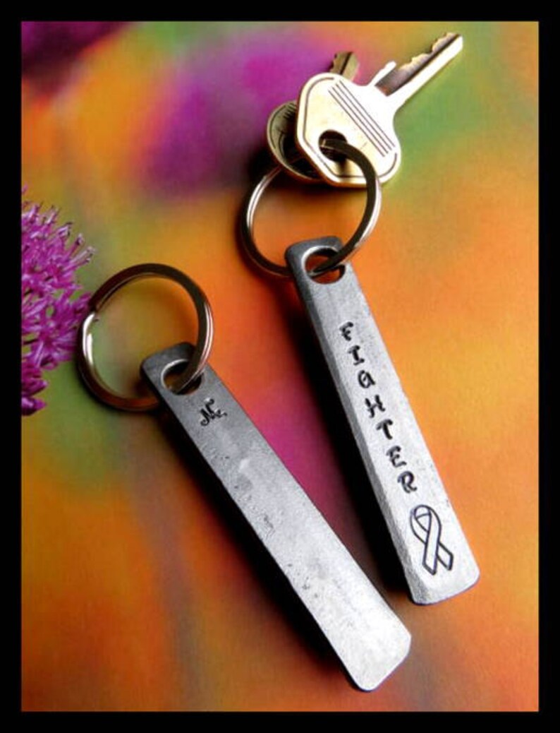 May include: Two silver keychains with key rings. One keychain has the word "Fighter" engraved on it with a ribbon design. The other keychain has the initials "J.C." engraved on it.