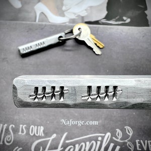 May include: A silver metal keychain with a key and a tag engraved with the words "Happily Ever After". The keychain is on a dark surface with a white background.