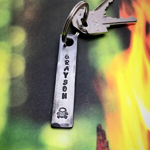 May include: A silver metal keychain with a skull and crossbones design and the name "GRAYSON" engraved on it.