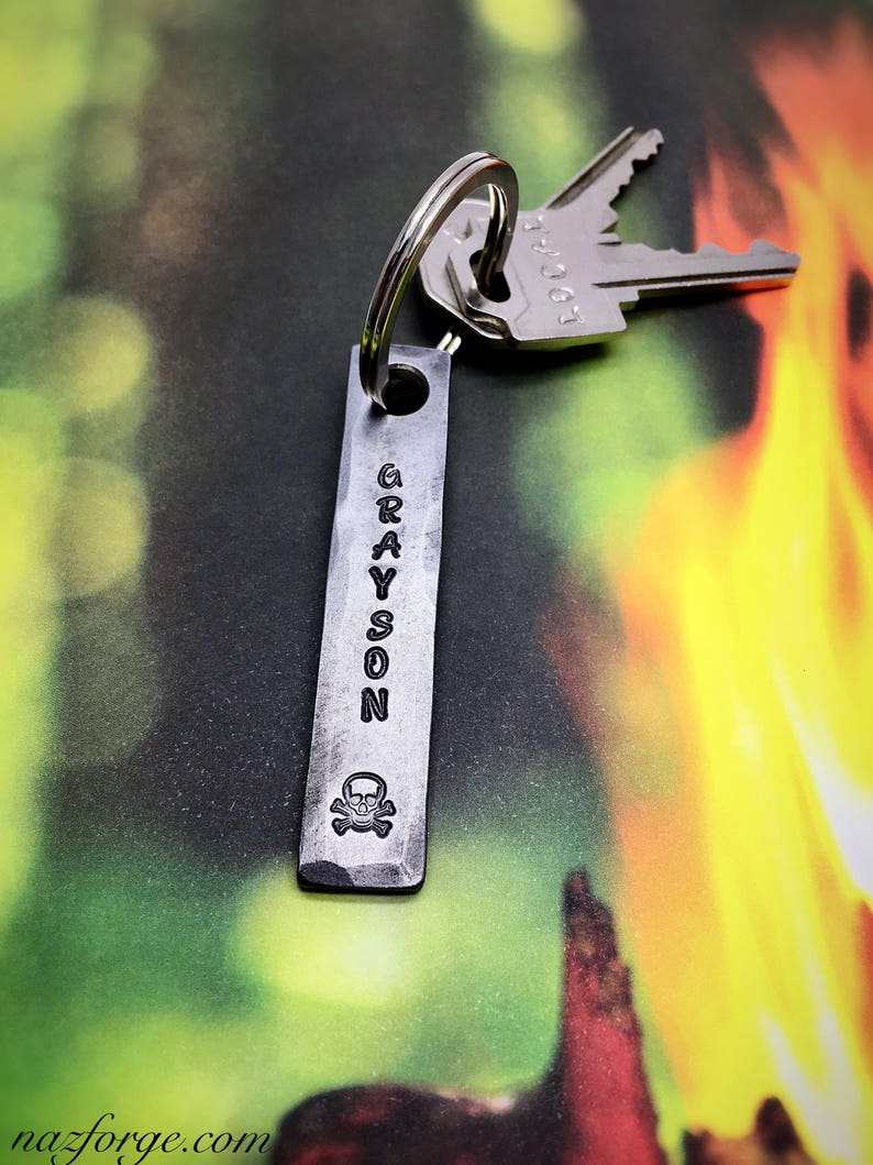 May include: A silver metal keychain with a skull and crossbones design and the name "GRAYSON" engraved on it.