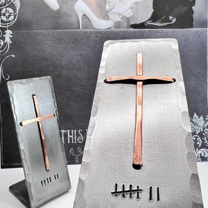 May include: Two hammered silver-toned metal stands, each featuring a vertical copper cross and a stamped tally mark design. The larger stand displays seven tally marks, while the smaller stand displays seven tally marks. The text Nazforge.com is visible.