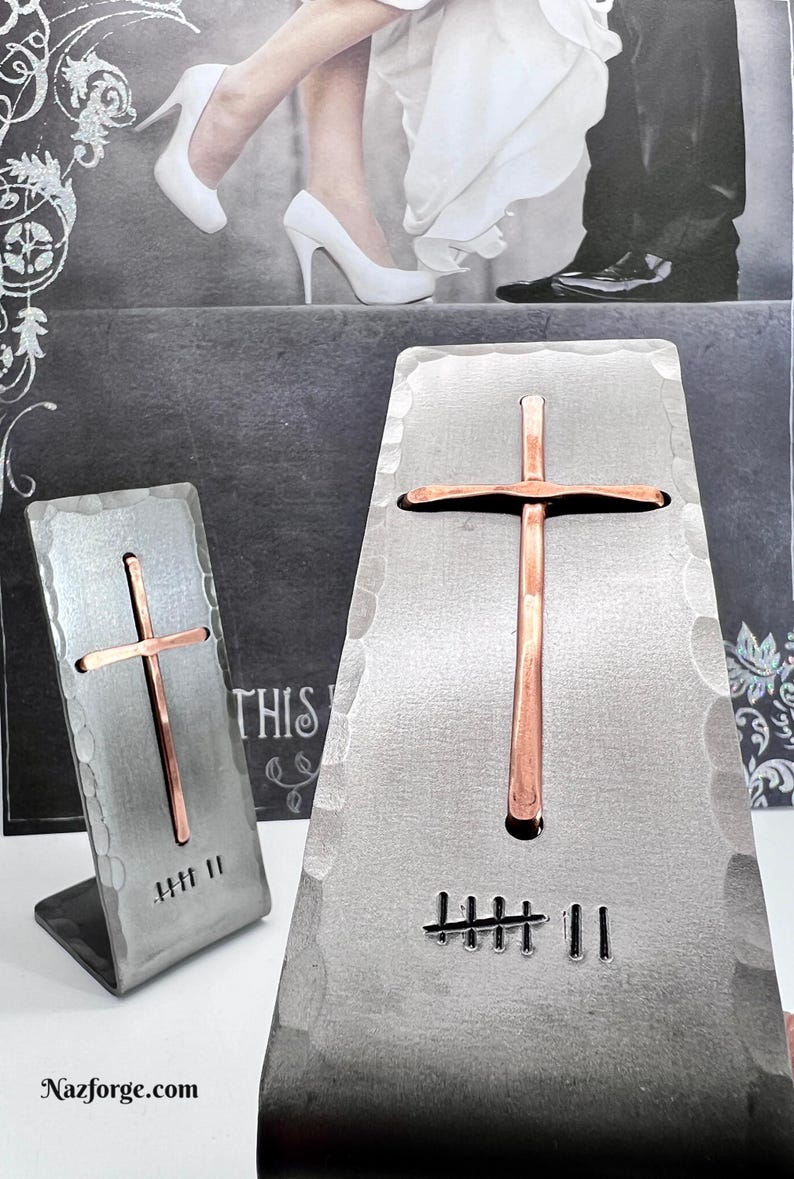 May include: Two hammered silver-toned metal stands, each featuring a vertical copper cross and a stamped tally mark design. The larger stand displays seven tally marks, while the smaller stand displays seven tally marks. The text Nazforge.com is visible.