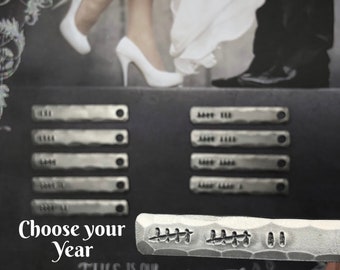 May include: A silver metal tag with the text "Choose your Year" and the year "2022" embossed on it. The tag is on a black background with the text "This is our Happily Ever After" written in white chalk.