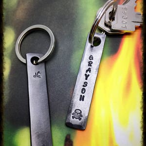May include: Two silver keychains with engraved names. The keychain on the left says "JC" and the keychain on the right says "GRAYSON" with a skull and crossbones symbol.