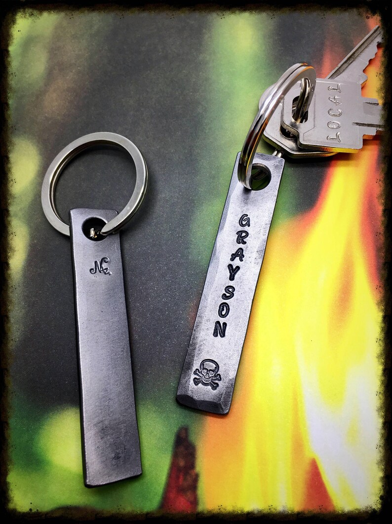 May include: Two silver keychains with engraved names. The keychain on the left says "JC" and the keychain on the right says "GRAYSON" with a skull and crossbones symbol.