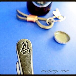 May include: A silver bottle opener with a peace sign engraved on the handle. The opener is on a blue surface.