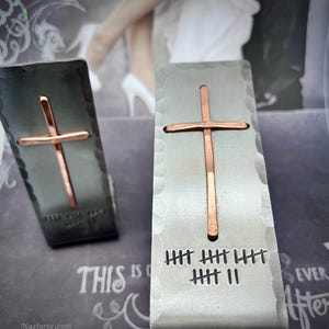 May include: Two silver metal wedding favors with a copper cross design. The favors have a hammered texture and the text "HHH HHH HHH HHH II" is engraved on the bottom.