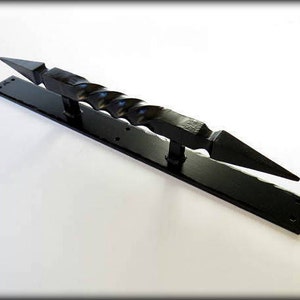 May include: Black metal door pull with a twisted design and pointed ends. The pull is mounted on a rectangular plate.
