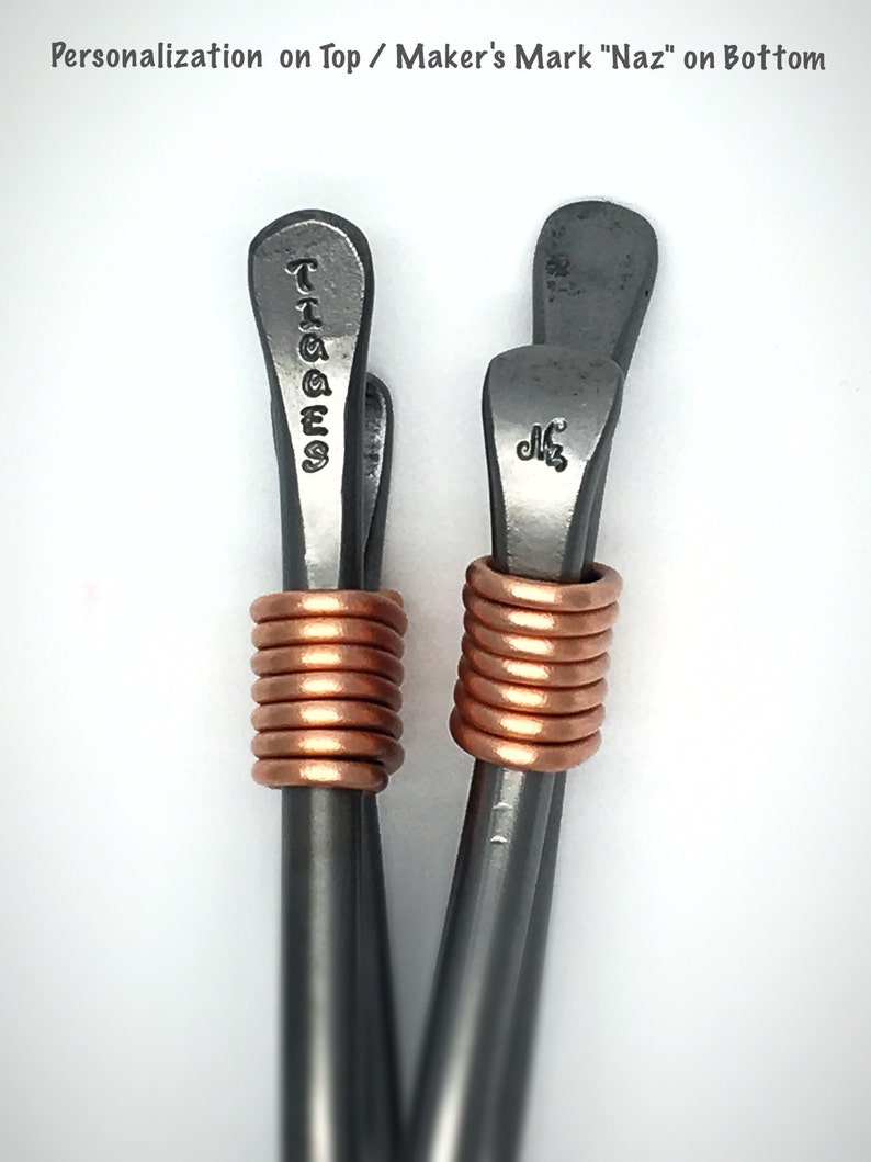 May include: Two silver metal hair clips with copper wire wrapped around the middle. The top of each clip has a personalized inscription. One clip says "TAGGES" and the other says "Naz".