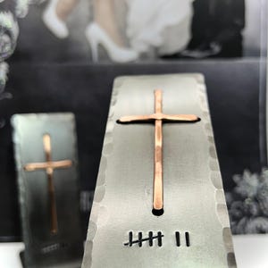 May include: Two rectangular, hammered metal stands featuring a centered, vertical copper cross. Each stand displays a hand-stamped tally mark design consisting of five vertical lines with a diagonal strike-through, followed by two additional vertical lines.