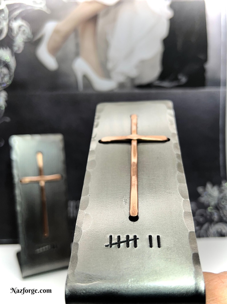May include: Two rectangular, hammered metal stands featuring a centered, vertical copper cross. Each stand displays a hand-stamped tally mark design consisting of five vertical lines with a diagonal strike-through, followed by two additional vertical lines.