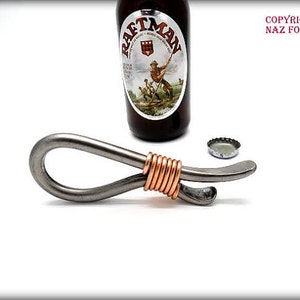 May include: A silver bottle opener with a copper wire wrapped around the handle. The bottle opener is on a white surface.