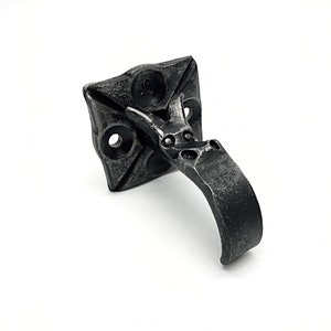 May include: Black metal hook with a square base and a curved handle. The hook is designed to be mounted to a wall or other surface.