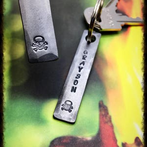 May include: Two metal keychains with a skull and crossbones design. One keychain has the name "GRAYSON" engraved on it.