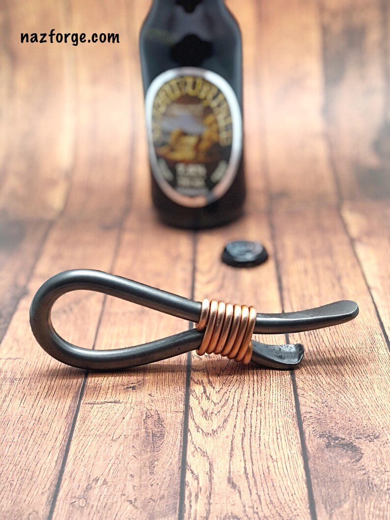 May include: A black metal bottle opener with a copper wire wrap. The opener has a loop on one end and a bottle opener on the other end.