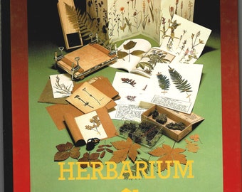 May include: A vintage herbarium kit with pressed flowers, botanical illustrations, and a wooden plant press. The cover features the word "HERBARIUM" in yellow letters on a green background, framed by red.