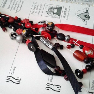 May include: A red, black, and white beaded keychain with a charm that says "Live". The keychain is attached to a key ring and has a black ribbon with a red ribbon attached to it.