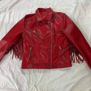 Pode incluir: Uma jaqueta de couro vermelha vibrante com gola clássica e fecho frontal com zíper. A jaqueta apresenta franjas nas mangas e vários bolsos com zíper. Esta elegante peça de roupa exterior é perfeita para adicionar uma declaração ousada a qualquer roupa.