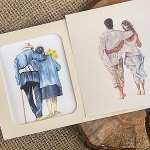 Op de afbeelding: Wenskaart met twee aquarel illustraties. Eén toont een ouder echtpaar met de armen om elkaar heen, de andere toont een stel dat hand in hand loopt. De kaart ligt op een jute oppervlak.