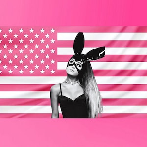 Puede incluir: Imagen en blanco y negro de una persona con una máscara de conejito y un top negro, sobre un fondo de bandera estadounidense rosa y blanca. La persona mira hacia arriba, con pelo largo y claro.