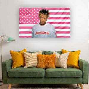 Könnte beinhalten: Gerahmter Druck mit einem Porträt einer Person in einem weißen Langarmshirt mit dem roten Text "JUICEWRLD", vor einer rosa amerikanischen Flagge. Der Druck hängt über einem grünen Sofa mit gelben und orangefarbenen Kissen.